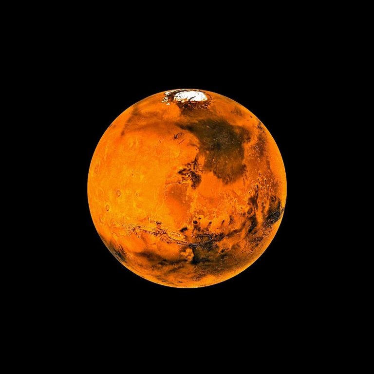 A rover traversing the red rocky surface of Mars with layered terrain and a dusty horizon behind it.